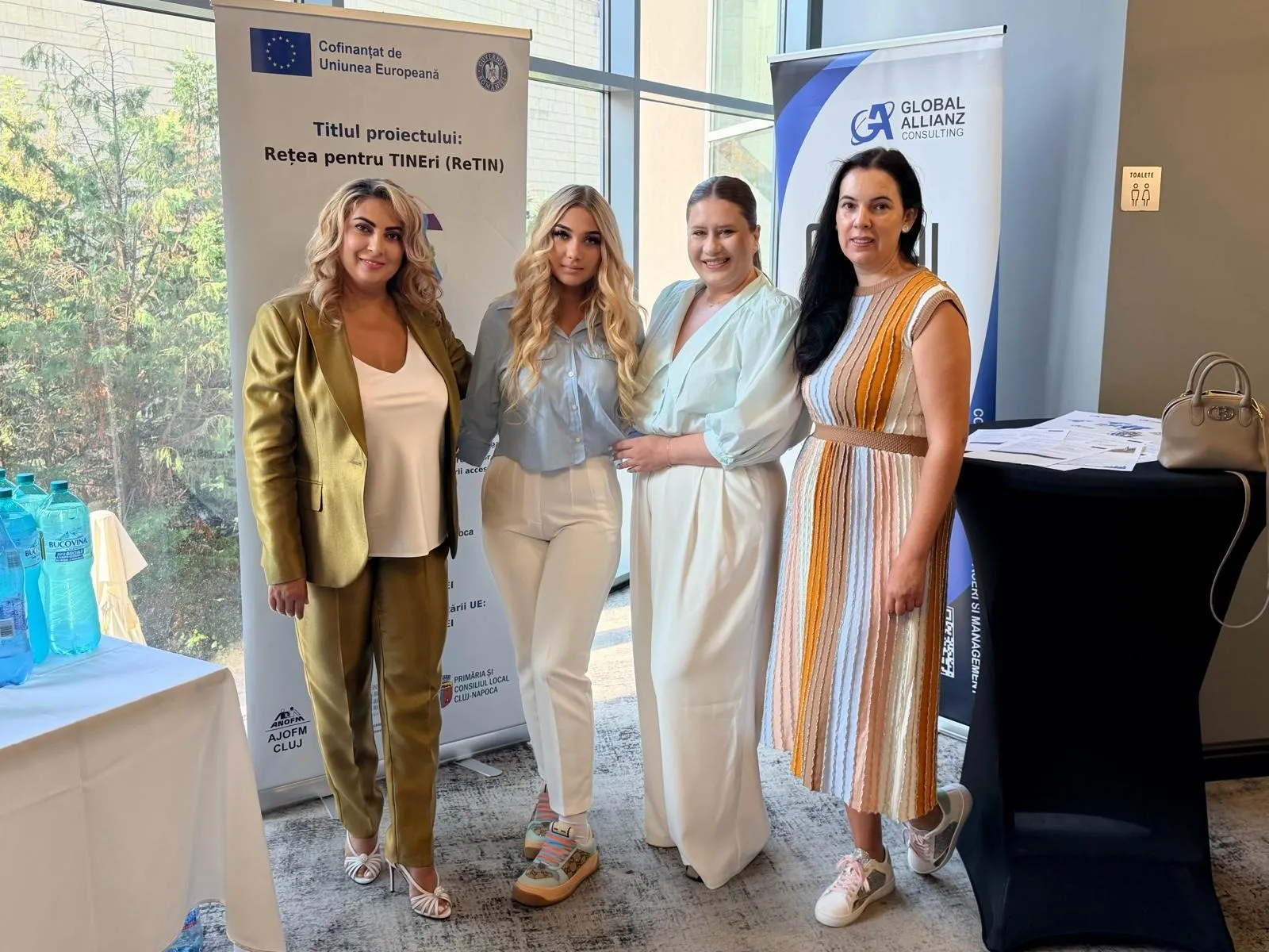 Patru doamne la evenimentul proiectului ReTIN, între bannerul proiectului cofinanțat de Uniunea Europeană și roll-up-ul Global Allianz Consulting.